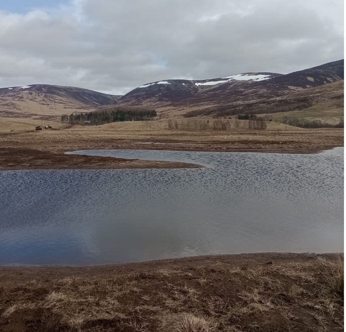 A small body of water infront of hills with a dusting of snow on them.