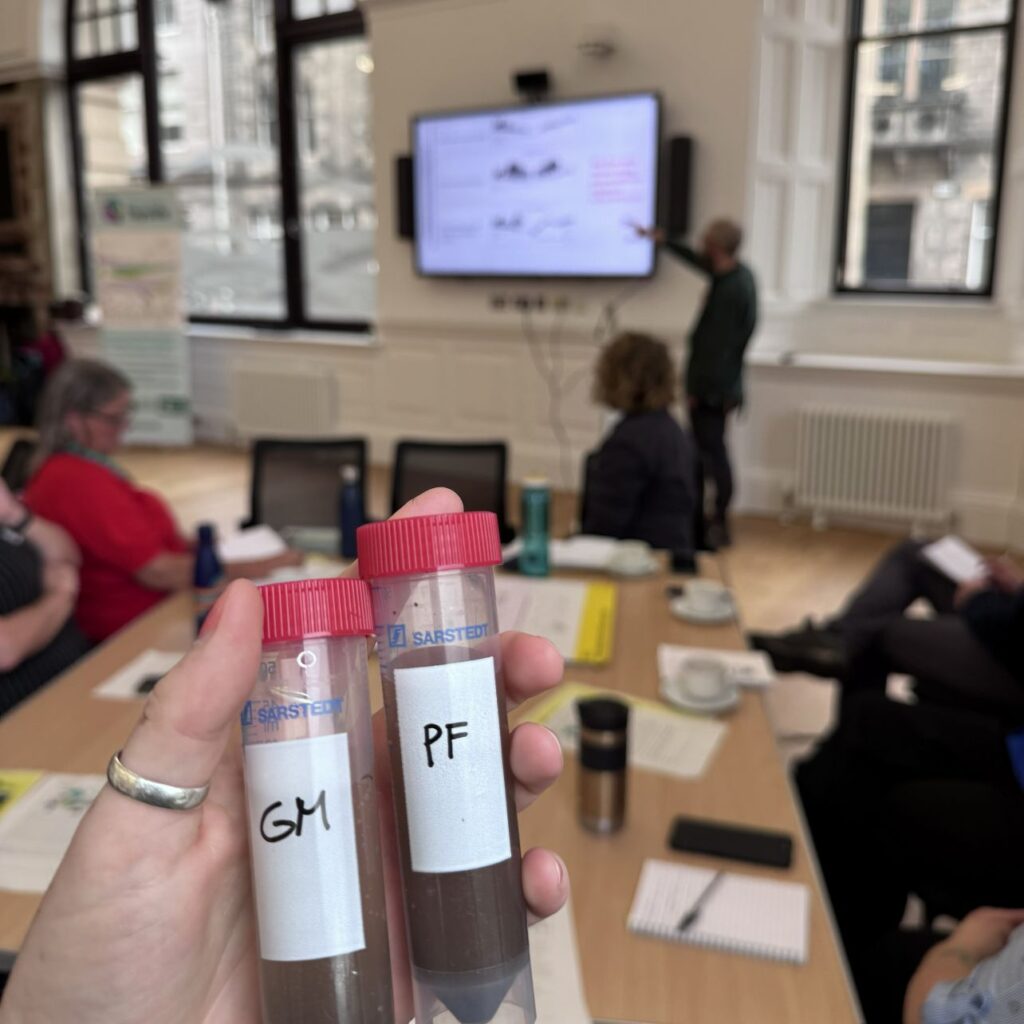 Two soil samples with water being held up to the camera with a presentation going on behind